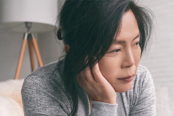 A middle-aged asian woman sitting on her couch, resting her head on her hand, suffering from adrenal fatigue. Get treatment for adrenal fatigue syndrome from Tanya Zboril, NP of TBT Medical in Edmonton.