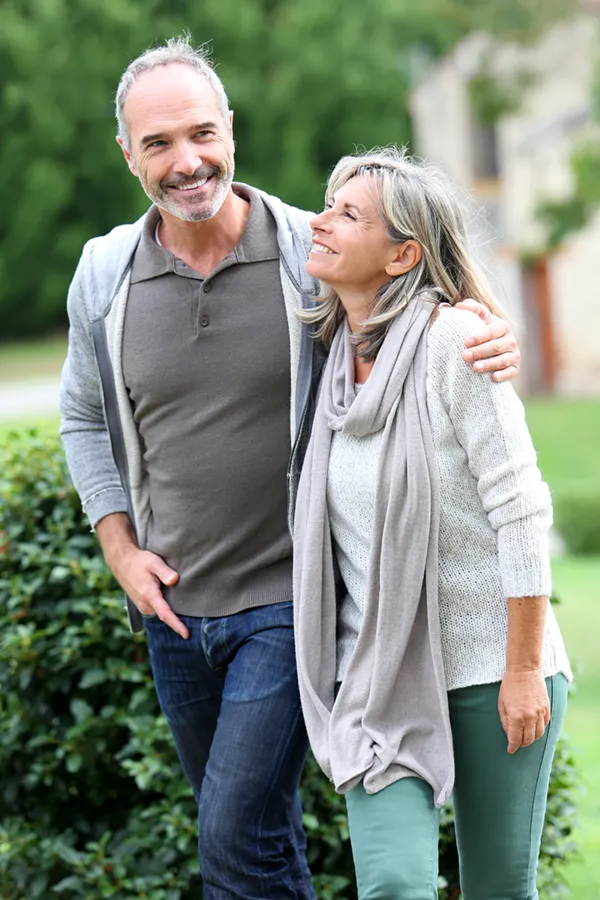 A mature couple in gray toned clothes and jeans walk happily outside, happy with their successful bioidentical hormone treatments from Tanya Zboril, NP of TBT Medical in Edmonton.