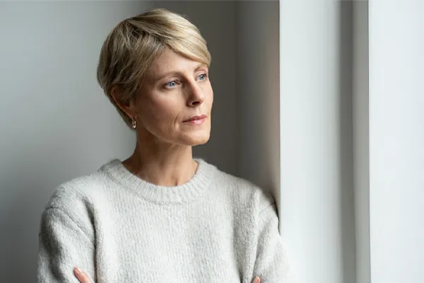 A blond, middle-aged woman looks out the window with a tired expression. Get chronic fatigue treatment from Tanya Zboril, NP of TBT Medical in Edmonton.