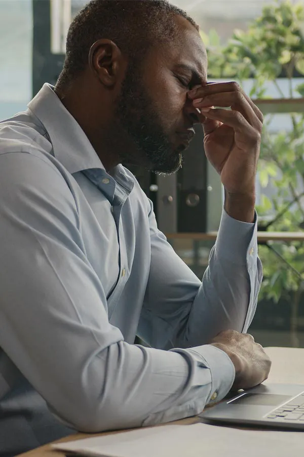 A black man rubbing the top of his nose at his desk, in need of chronic fatigue treatment from Tanya Zboril, NP of TBT Medical in Edmonton.