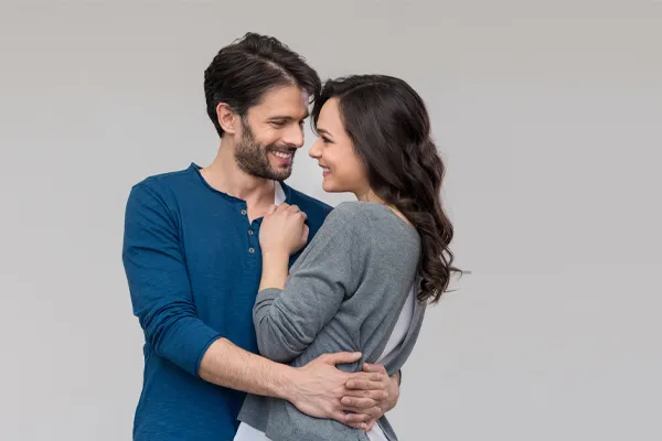 A man in a blue shirt embracing a woman in a gray shirt smiles due to his successful erectile dysfunction care from Tanya Zboril, NP of TBT Medical in Edmonton.