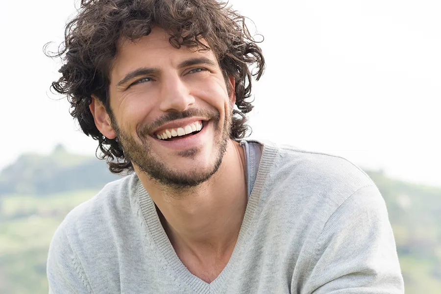 A man with radiant curly hair and a confident smile looks to the horizon. Tanya Zboril, NP of TBT Medical in Edmonton offers effective therapies to support hair regrowth and scalp health to treat hair loss.