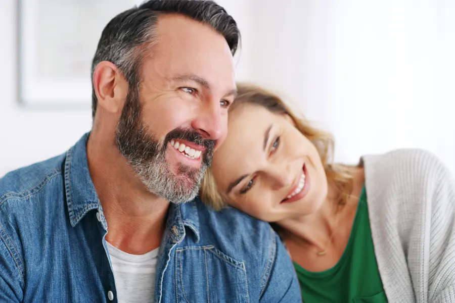 A middle-aged white couple in a bright white room smile and lay their heads on each other. Schedule concierge health and wellness services from Tanya Zboril, NP of TBT Medical in Edmonton.