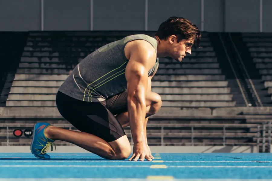 A white man kneels at the starting line on a track, determined to do his best. Get treatment for lean muscle loss and recovery from Tanya Zboril, NP of TBT Medical in Edmonton.