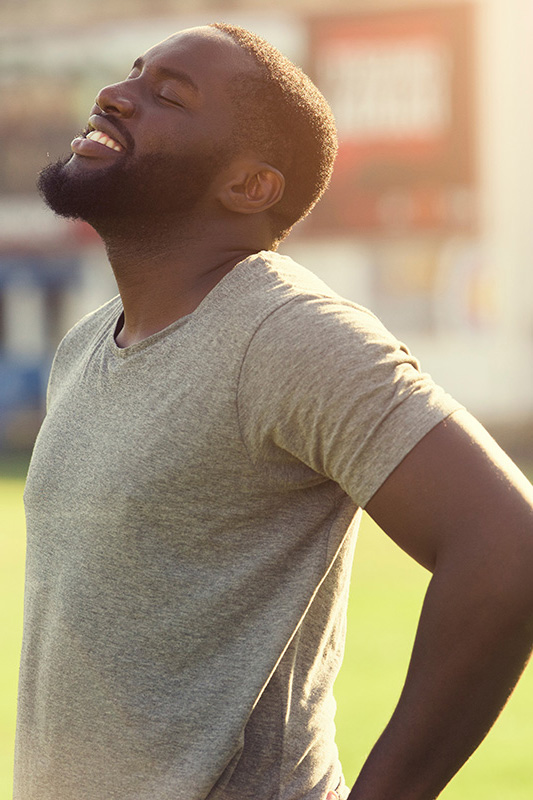 A black man in a gray t-shirt and smiles, looking up with closed eyes after a satisfying workout. Get treatment for lean muscle loss and recovery from Tanya Zboril, NP of TBT Medical in Edmonton.