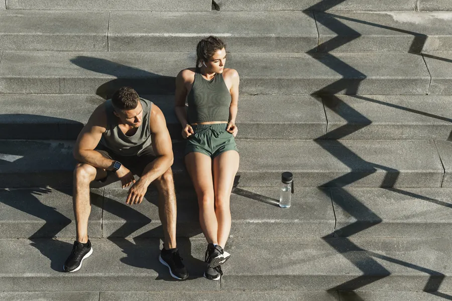 Medical-Weight-Loss-Doctor A couple in gray and green track clothes resting after a workout on stone steps, happy with their weight loss plans from Tanya Zboril, NP of TBT Medical in Edmonton.