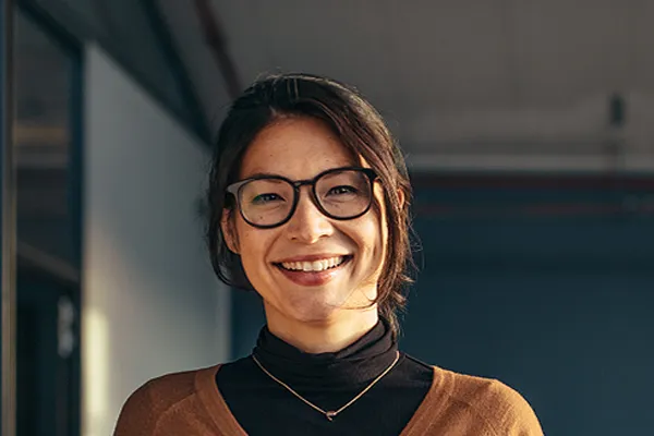 A brunette woman with glasses smiles in a gray-blue walled office. Get metabolic syndrome from Tanya Zboril, NP of TBT Medical in Edmonton.
