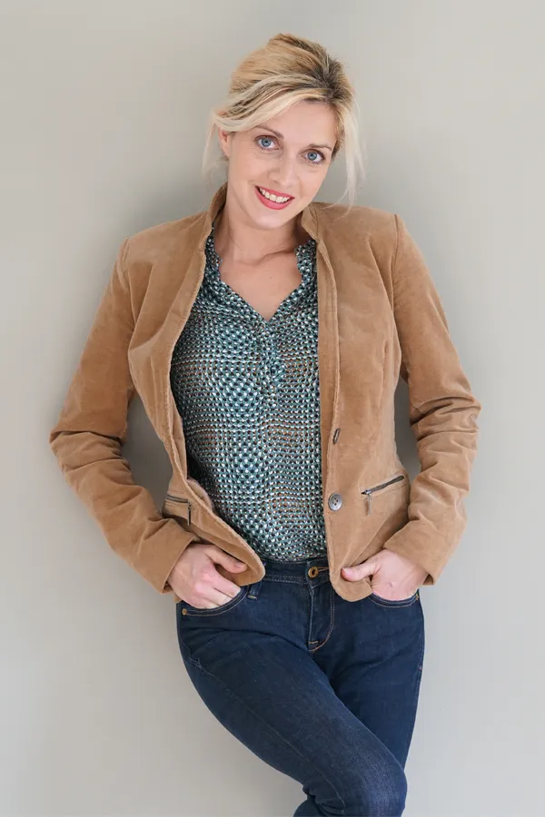 A smiling blonde woman in a tan leather jacket leans against a gray wall. Schedule metabolic syndrome from Tanya Zboril, NP of TBT Medical in Edmonton.