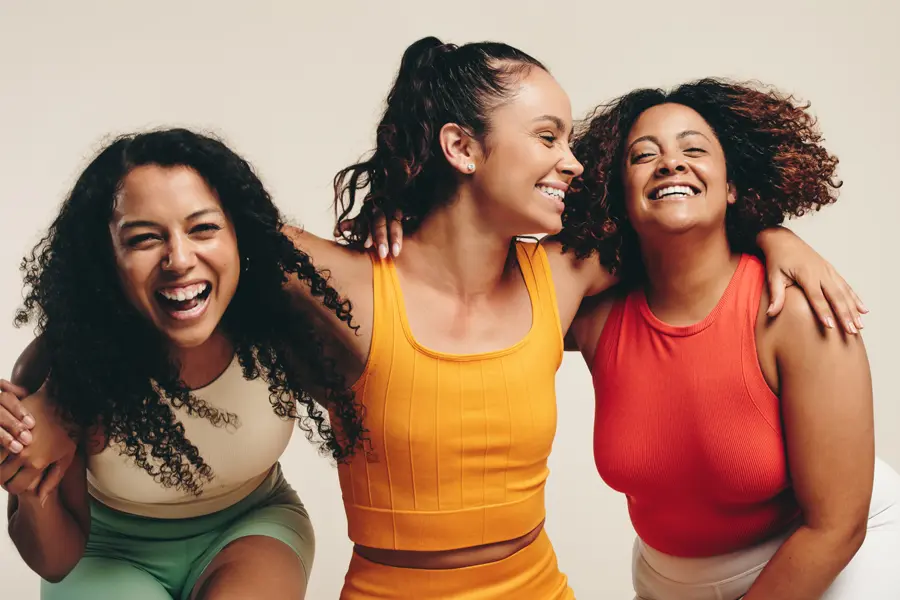 Three healthy women in colorful clothes laugh arm in arm. Schedule Mounjaro for weight loss from Tanya Zboril, NP of TBT Medical in Edmonton.