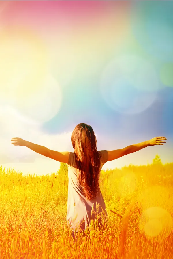 Ottawa-NAD-Therapy-Treatment Woman standing in a golden field with arms outstretched toward a vibrant, rainbow-hued sky, symbolizing vitality and inner renewal with NAD Therapy offered by Tanya Zboril, NP of TBT Medical in Edmonton.
