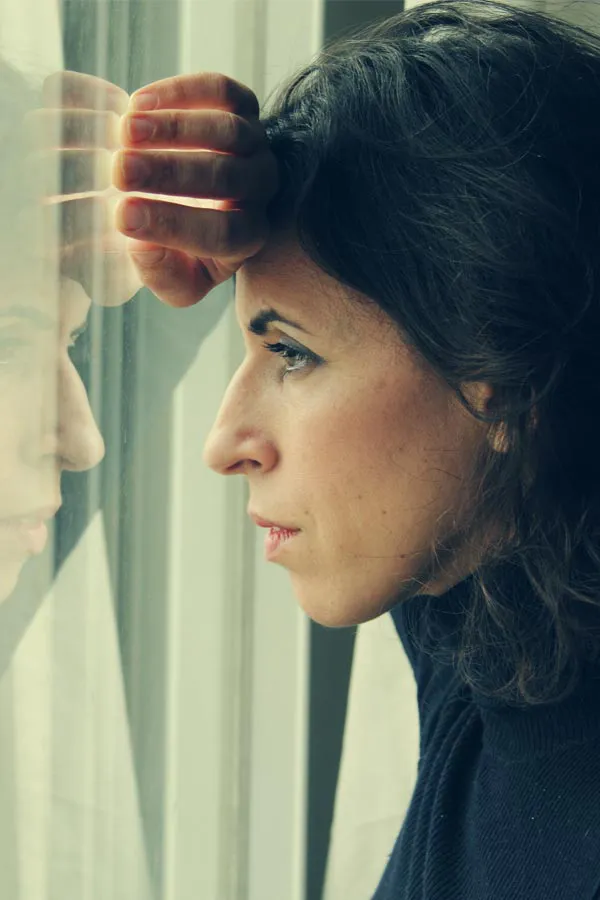 A brunette woman in a thin dark turtleneck looks out the window with a serious expression, suffering from PCOS. Get treatment for Polycistic Ovarian Syndrome/PCOS from Tanya Zboril, NP of TBT Medical in Edmonton.