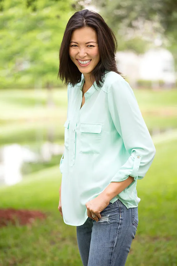 A middle-aged brunette woman in a light green button-up shirt stands outside smiling, happy with her perimenopause treatment from Tanya Zboril, NP of TBT Medical in Edmonton.