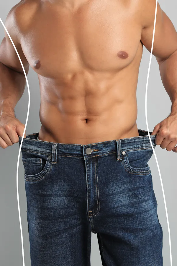 A strong shirtless man in jeans holds the waistlines of his too-big jeans to show the success of semaglutide weight loss from Tanya Zboril, NP of TBT Medical in Edmonton.