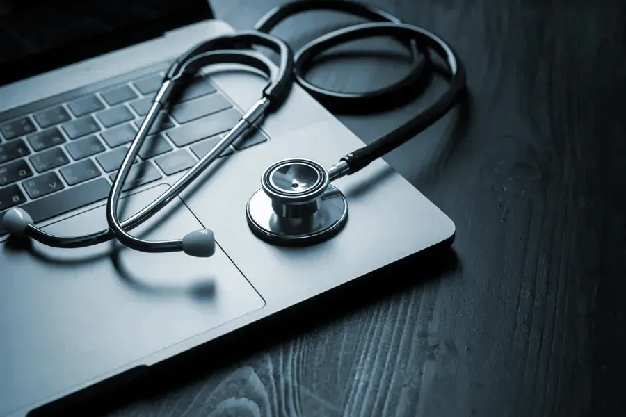 Telemedicine-Doctor An open laptop with a stethoscope lying on it on a wooden table, symbolizing telemedicine care from Tanya Zboril, NP of TBT Medical in Edmonton.
