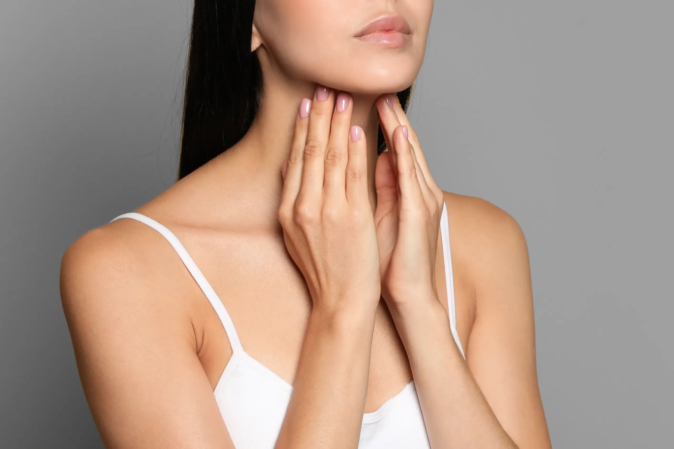 A woman in a white tank top touches her neck looking for signs of thyroid disorder. Get help for thyroid disorders from Tanya Zboril, NP of TBT Medical in Edmonton.