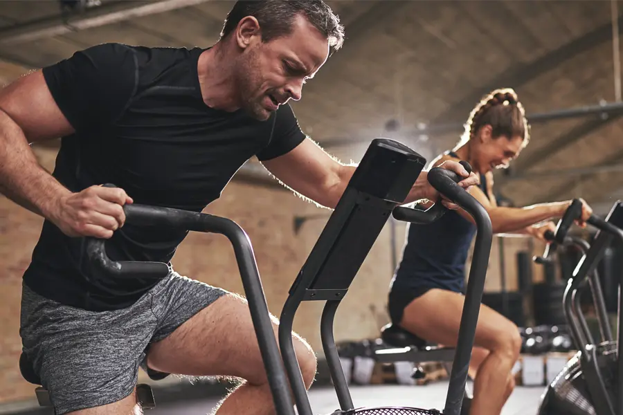 Tirzepatide-Doctor A couple in a brick gym work as hard as they can on exercise bikes, inspired by successful Tirzepatide treatment from Tanya Zboril, NP of TBT Medical in Edmonton.