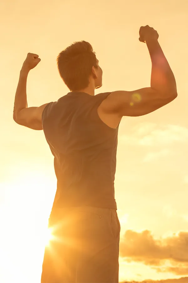 A motivational image of a young man standing with his back to the camera, arms raised triumphantly against a sunrise. Representing Wegovy Weight Loss Injections offered by Tanya Zboril, NP of TBT Medical in Edmonton.